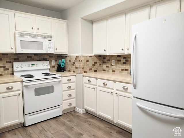 Kitchen with white cabinetry, white appliances, and light wood-type flooring