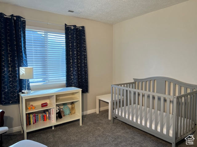 Bedroom with a crib, a textured ceiling, and dark carpet