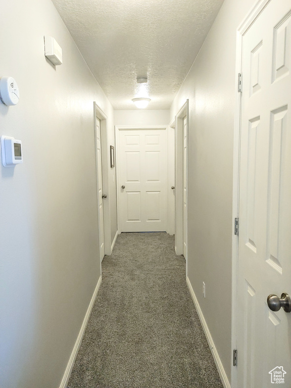 Corridor featuring dark colored carpet and a textured ceiling