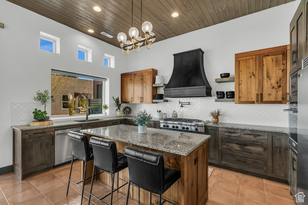 Kitchen featuring light stone countertops, premium range hood, wood ceiling, dishwasher, and an inviting chandelier