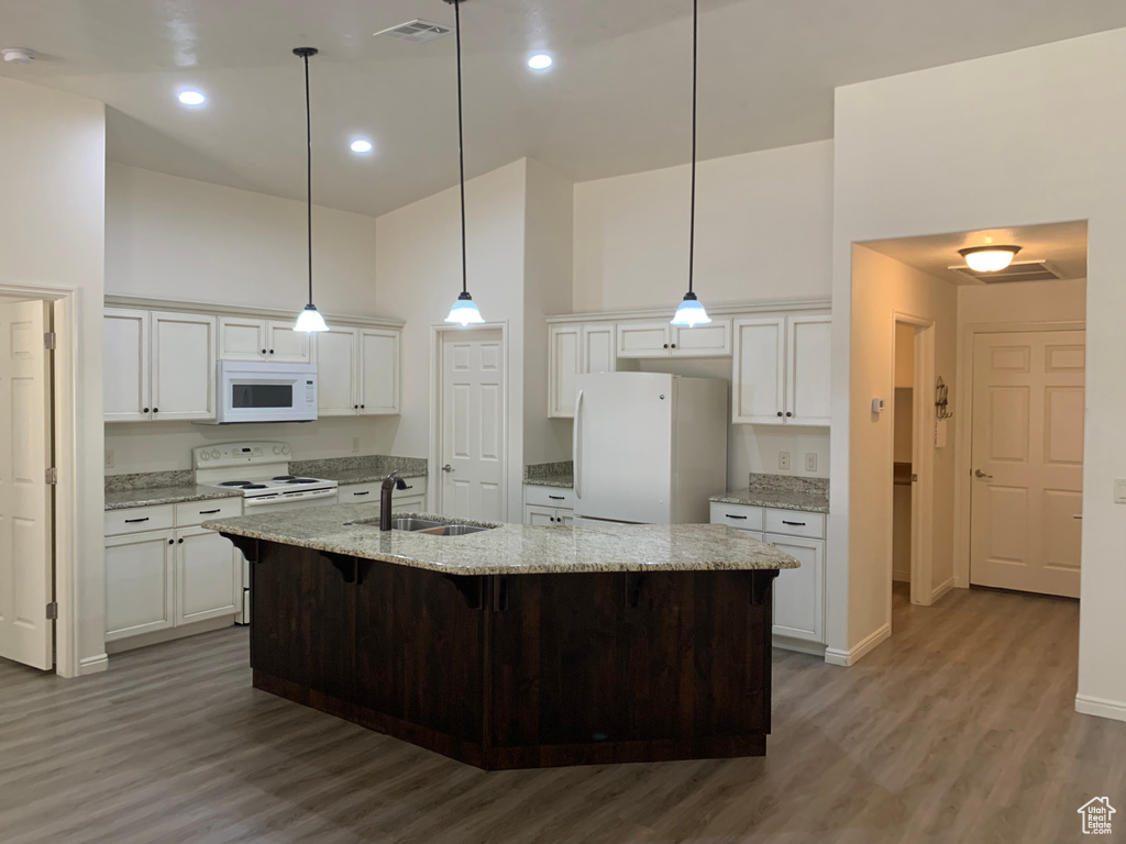 Kitchen with white appliances, sink, light hardwood / wood-style flooring, decorative light fixtures, and a high ceiling