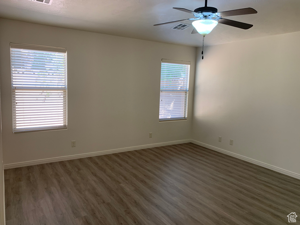 Empty room featuring dark hardwood / wood-style flooring, a wealth of natural light, and ceiling fan