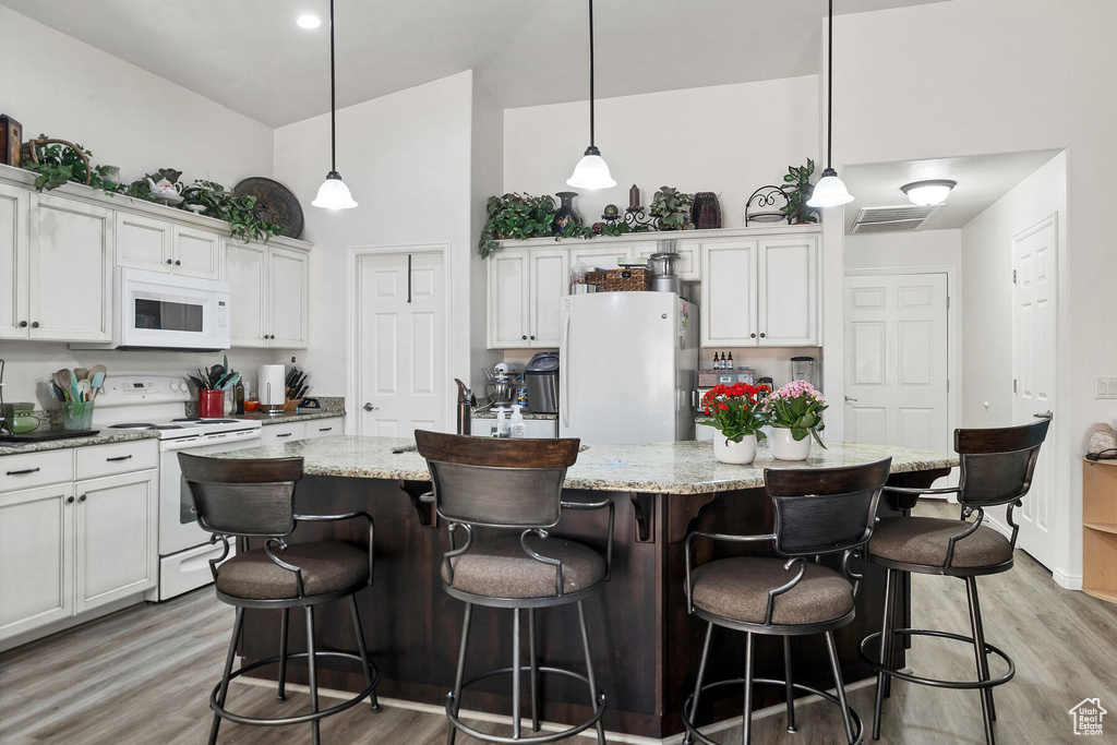 Kitchen with hanging light fixtures, light hardwood / wood-style flooring, white appliances, and a center island with sink