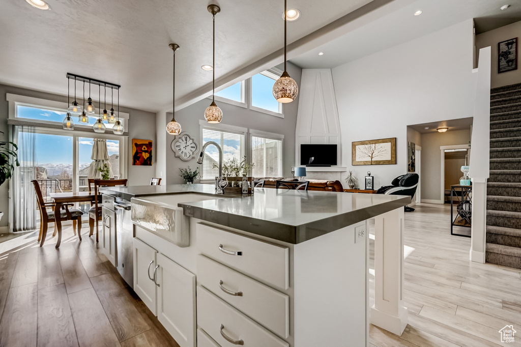 Kitchen featuring white cabinetry, pendant lighting, an island with sink, a high ceiling, and light wood-type flooring