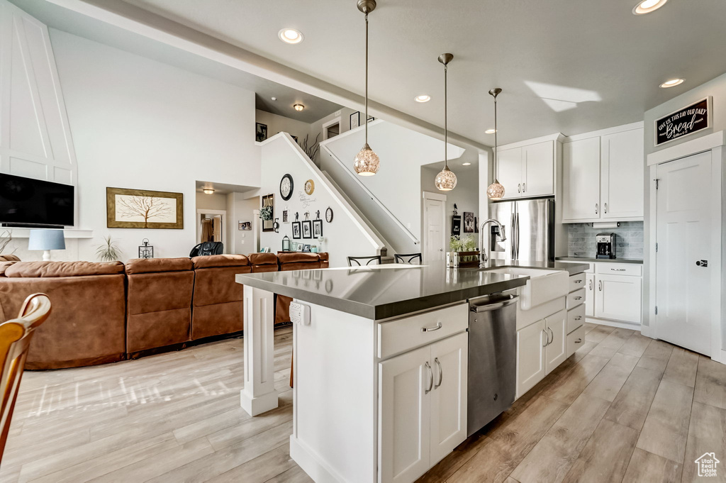Kitchen with white cabinets, appliances with stainless steel finishes, light wood-type flooring, and decorative light fixtures