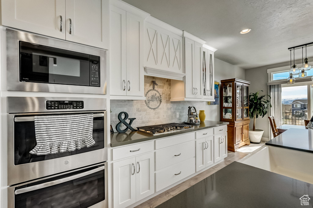 Kitchen featuring tasteful backsplash, white cabinets, stainless steel appliances, light hardwood / wood-style flooring, and pendant lighting