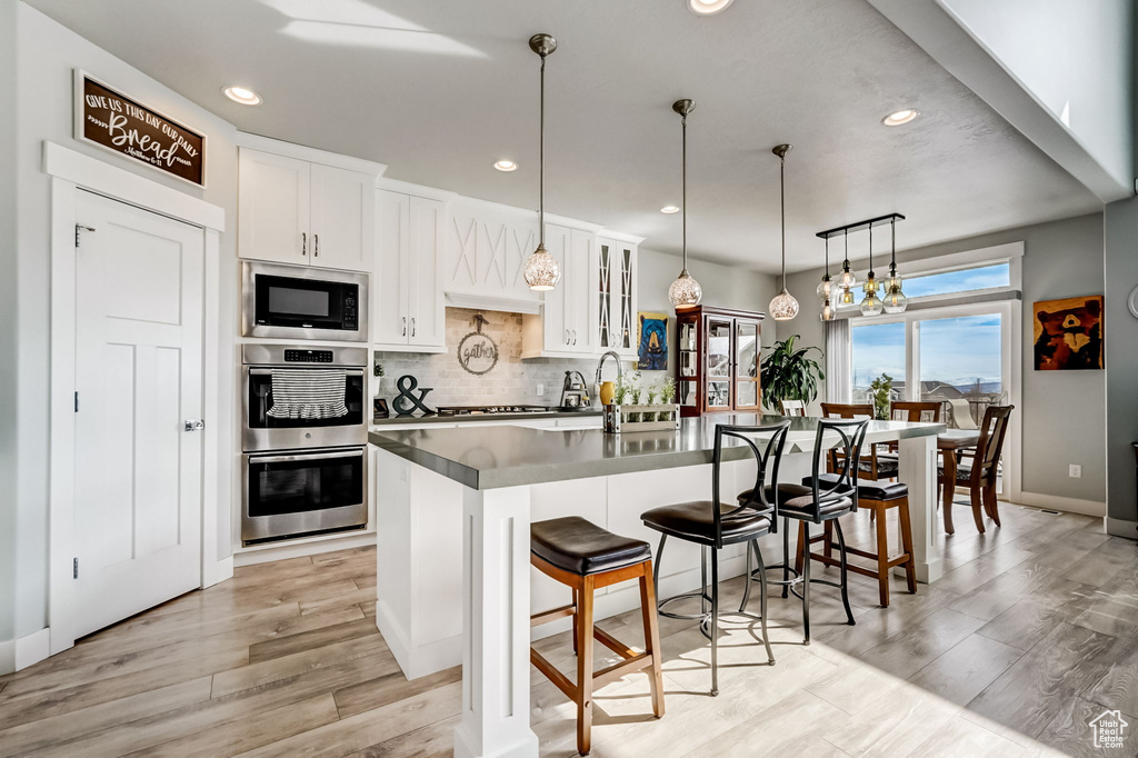 Kitchen featuring appliances with stainless steel finishes, white cabinetry, decorative light fixtures, and light hardwood / wood-style floors