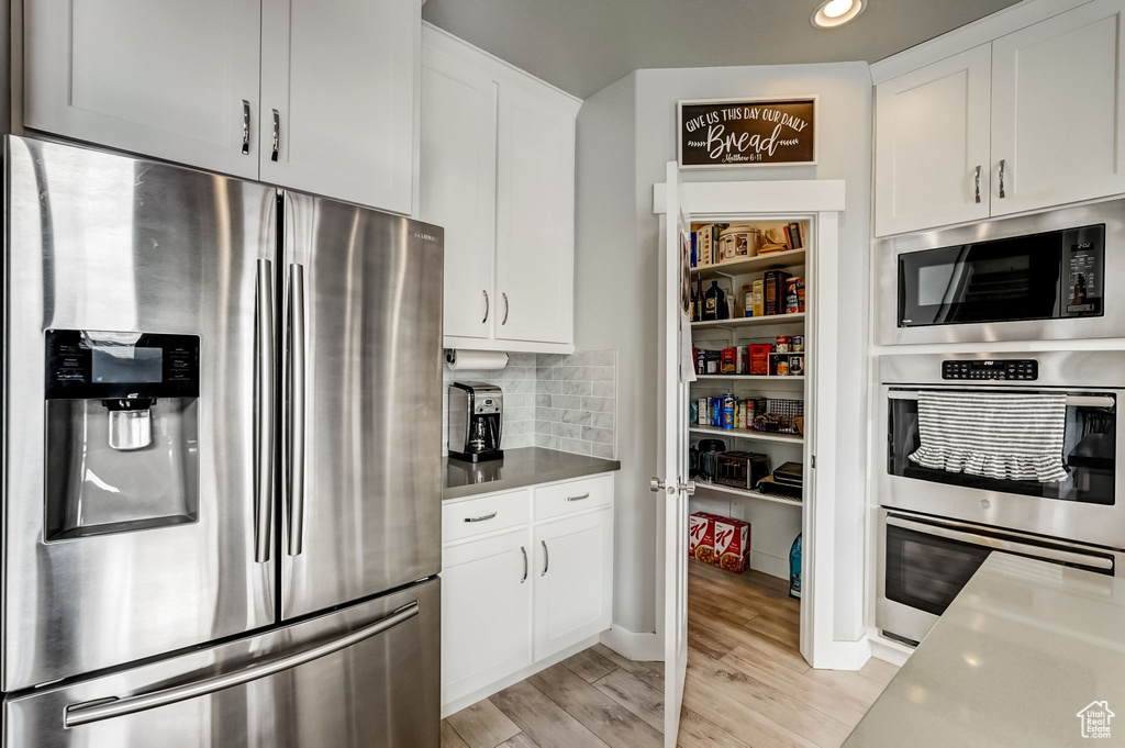 Kitchen with white cabinets, backsplash, light wood-type flooring, stainless steel appliances, and stainless steel counters
