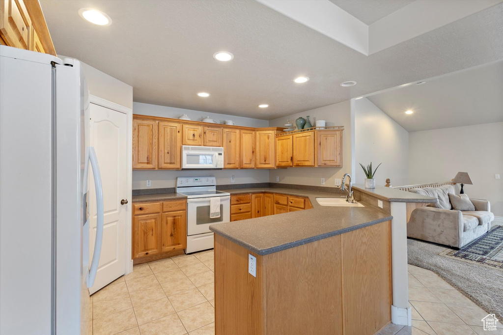 Kitchen featuring kitchen peninsula, light tile floors, a kitchen breakfast bar, white appliances, and sink