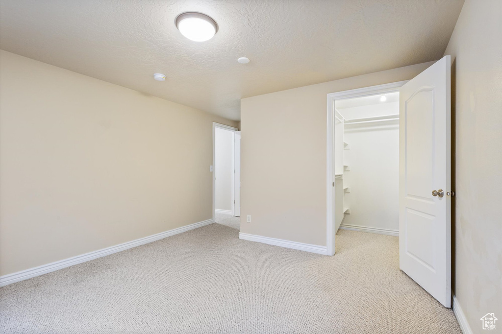 Unfurnished bedroom with light colored carpet, a spacious closet, a textured ceiling, and a closet