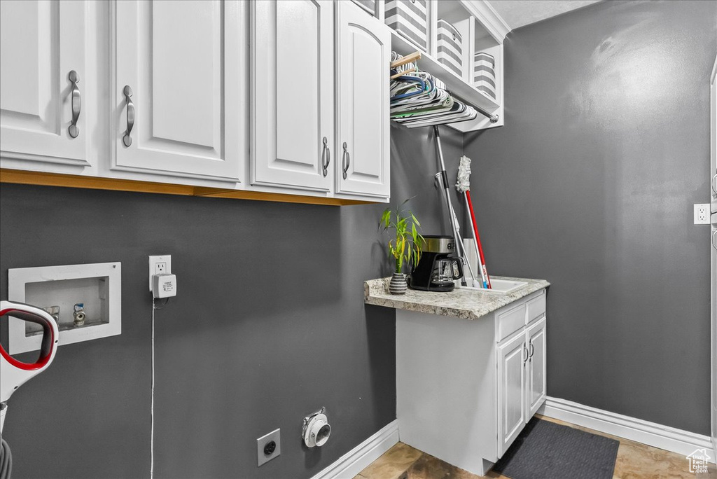 Interior space featuring hookup for an electric dryer, cabinets, hookup for a washing machine, and light tile flooring