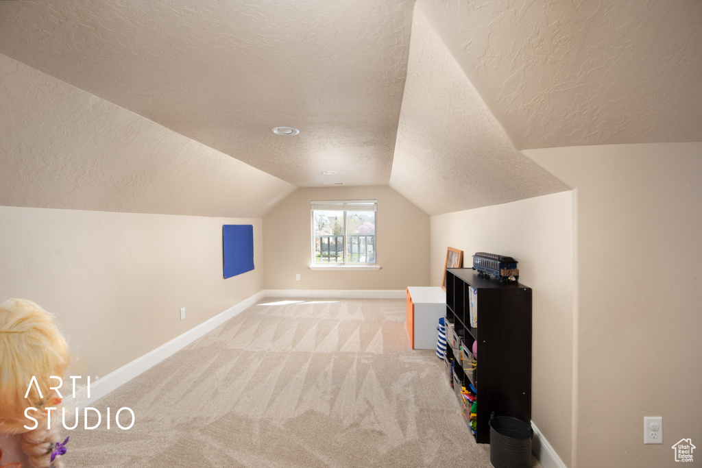 Additional living space featuring light colored carpet, a textured ceiling, and lofted ceiling