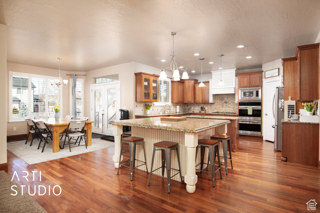 Kitchen featuring an inviting chandelier, hardwood / wood-style floors, pendant lighting, and appliances with stainless steel finishes