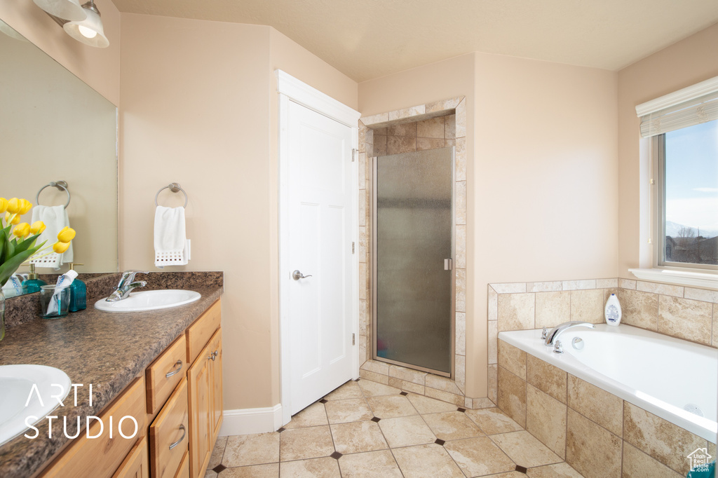 Bathroom featuring dual sinks, plus walk in shower, vanity with extensive cabinet space, and tile floors