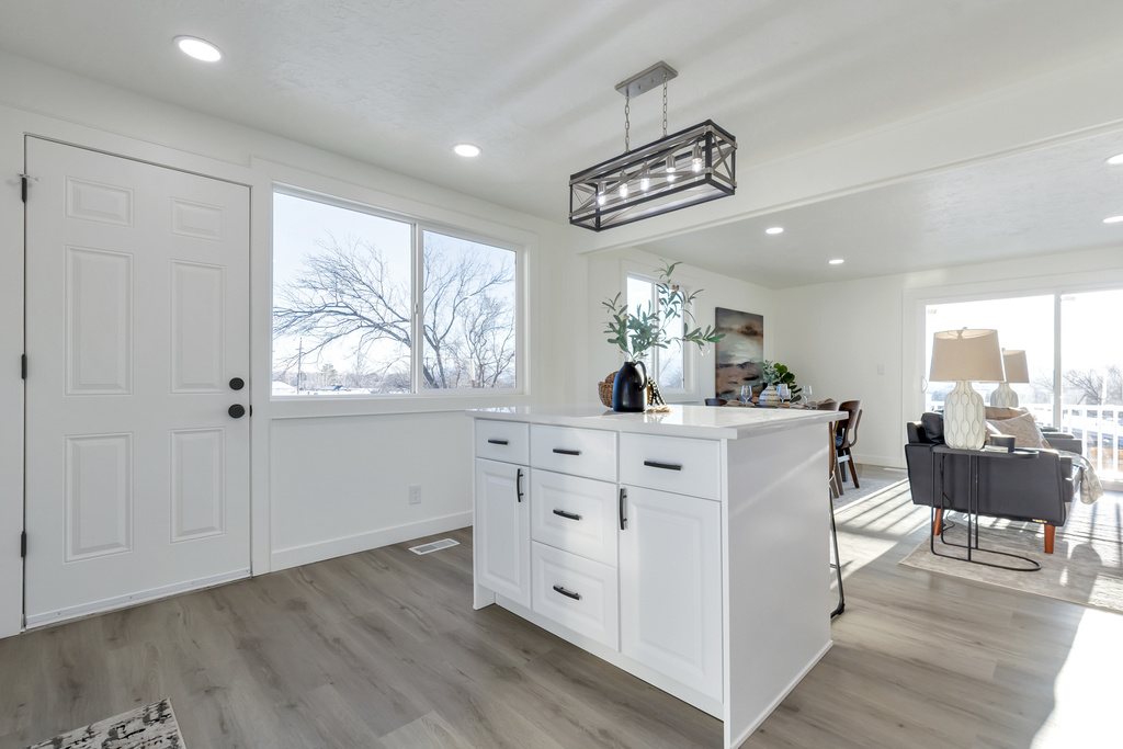 Kitchen featuring white cabinetry, light wood-type flooring, pendant lighting, and a healthy amount of sunlight