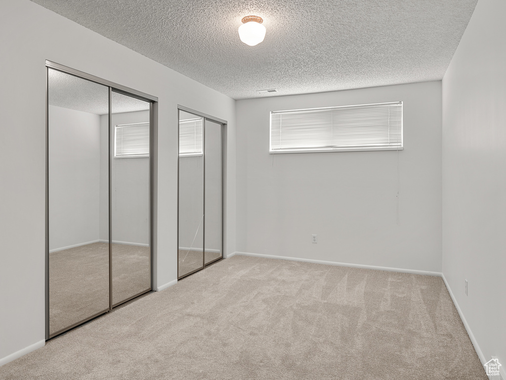 Unfurnished bedroom with light colored carpet, a textured ceiling, and two closets