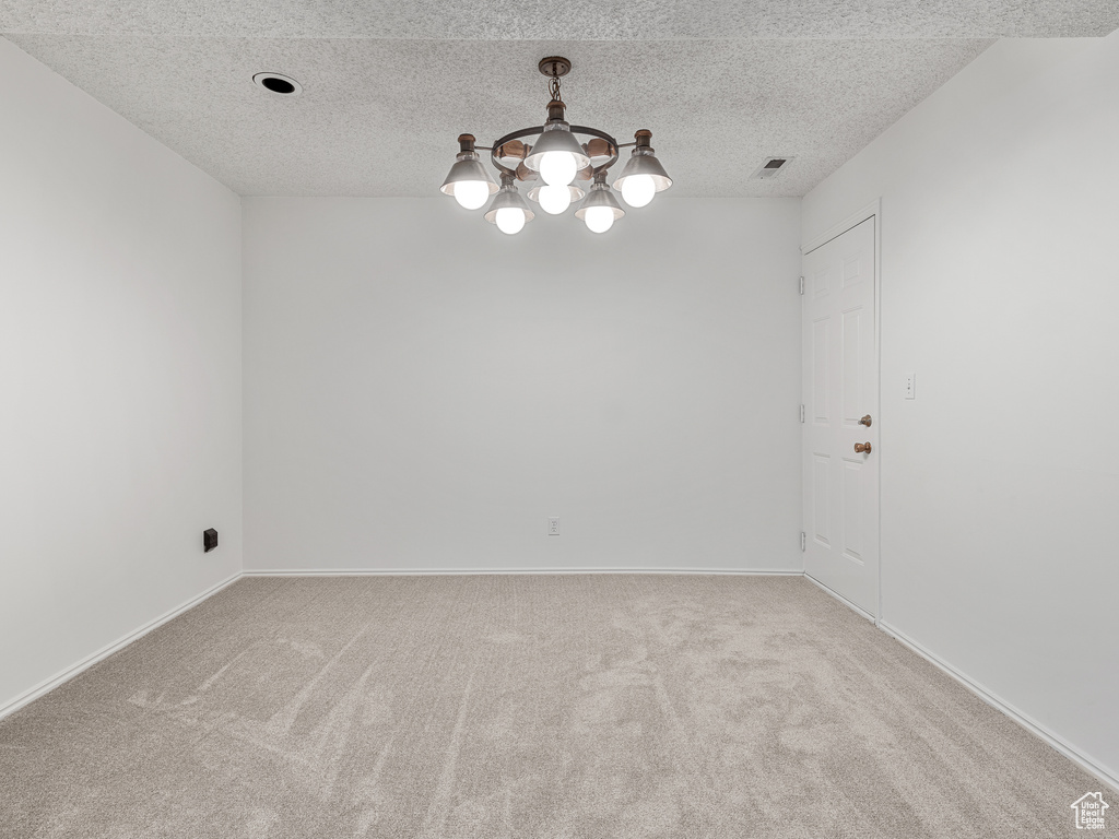Carpeted empty room featuring an inviting chandelier and a textured ceiling