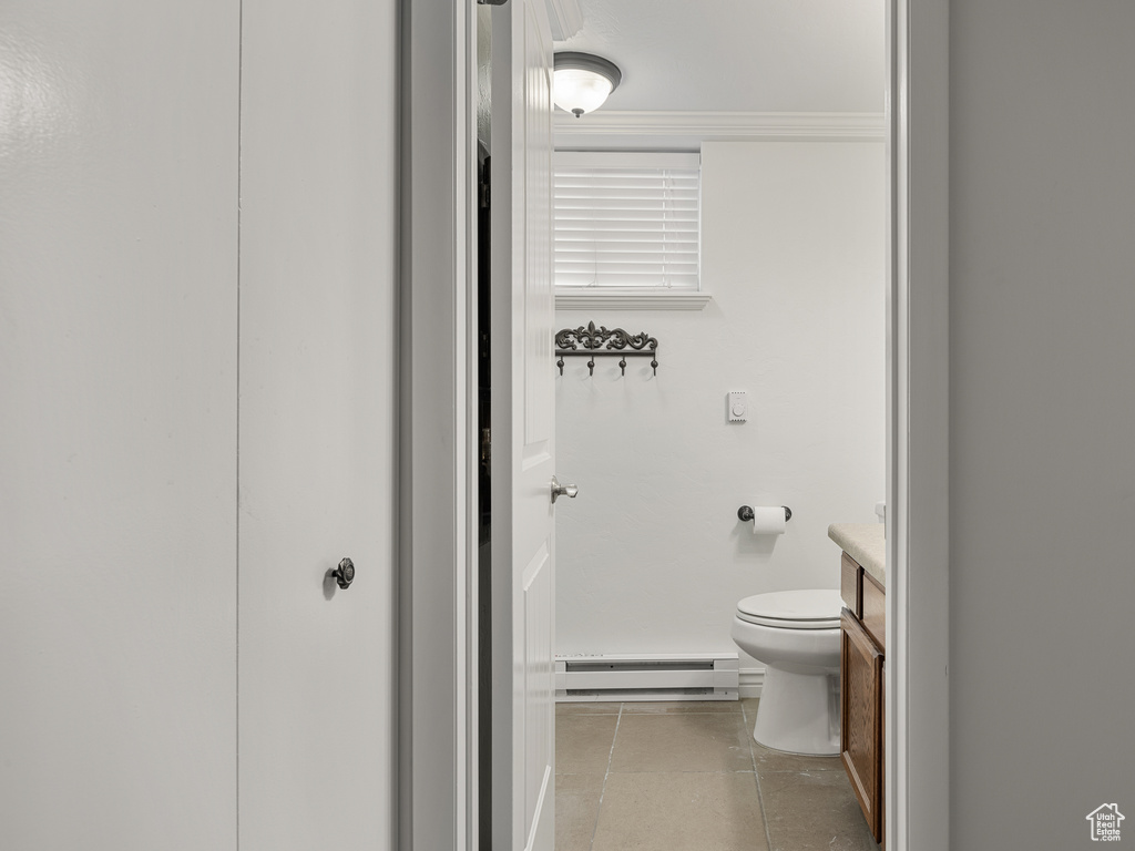 Bathroom with a baseboard radiator, toilet, vanity, and tile flooring