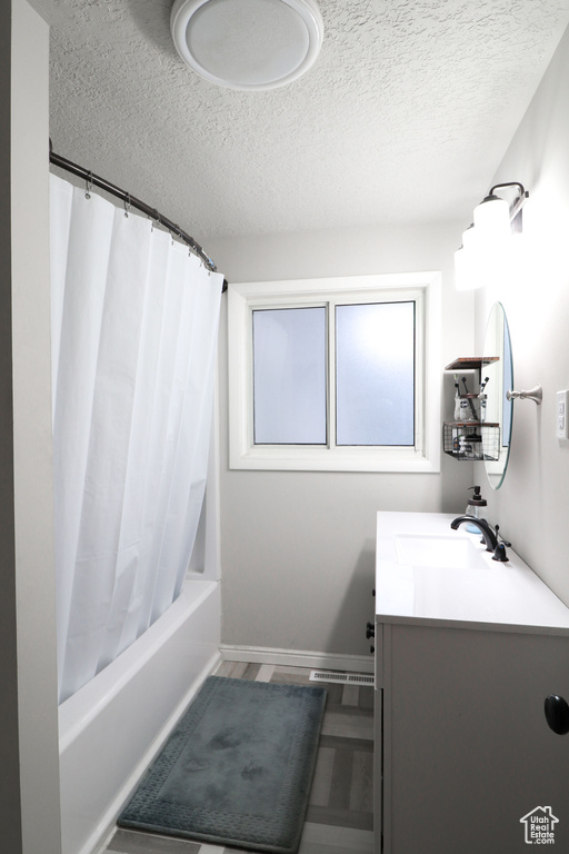 Bathroom with shower / bath combination with curtain, a textured ceiling, and vanity with extensive cabinet space
