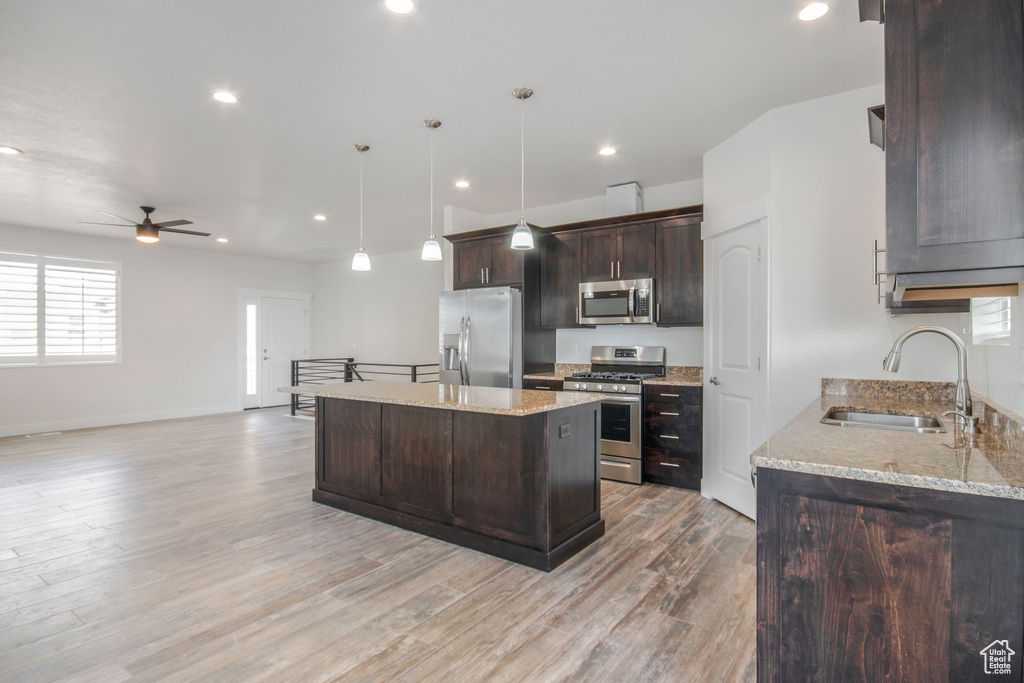 Kitchen featuring appliances with stainless steel finishes, light hardwood / wood-style floors, sink, hanging light fixtures, and light stone countertops
