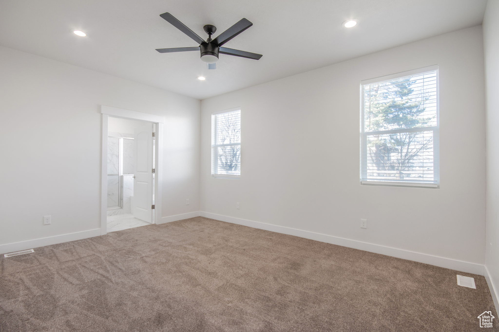 Empty room featuring light carpet, ceiling fan, and plenty of natural light