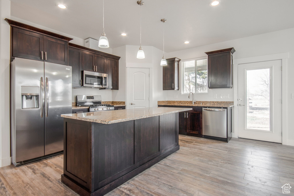 Kitchen featuring hanging light fixtures, appliances with stainless steel finishes, a kitchen island, light hardwood / wood-style flooring, and light stone counters