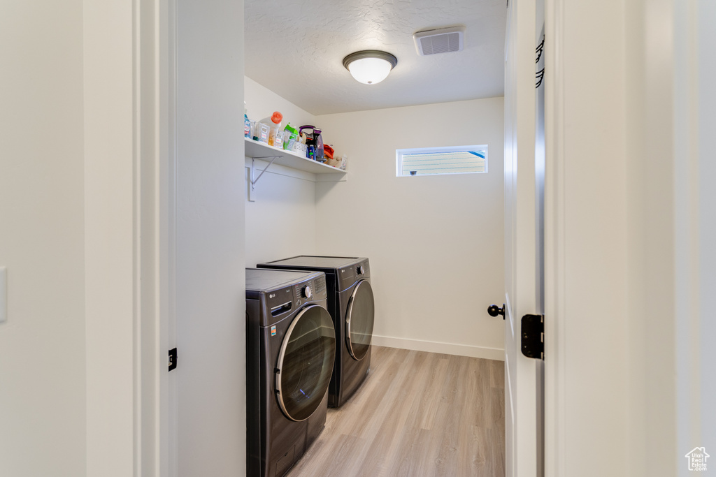 Laundry area with washer and clothes dryer and light hardwood / wood-style floors