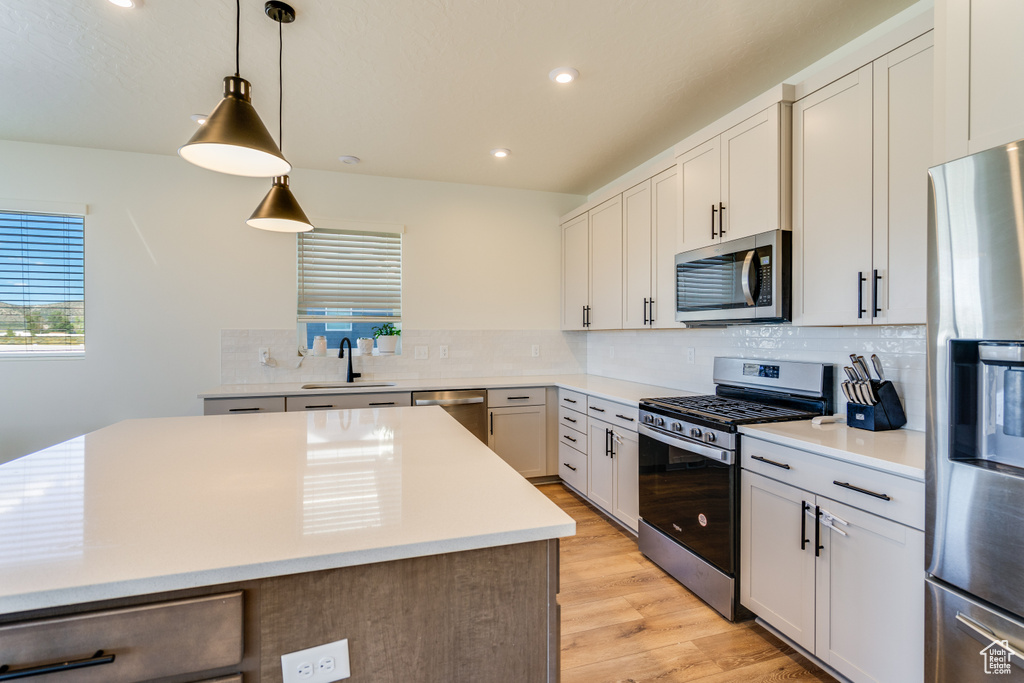 Kitchen with tasteful backsplash, stainless steel appliances, white cabinetry, light hardwood / wood-style flooring, and pendant lighting