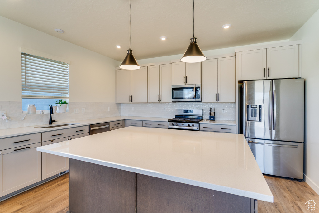 Kitchen featuring backsplash, appliances with stainless steel finishes, sink, light hardwood / wood-style flooring, and a center island