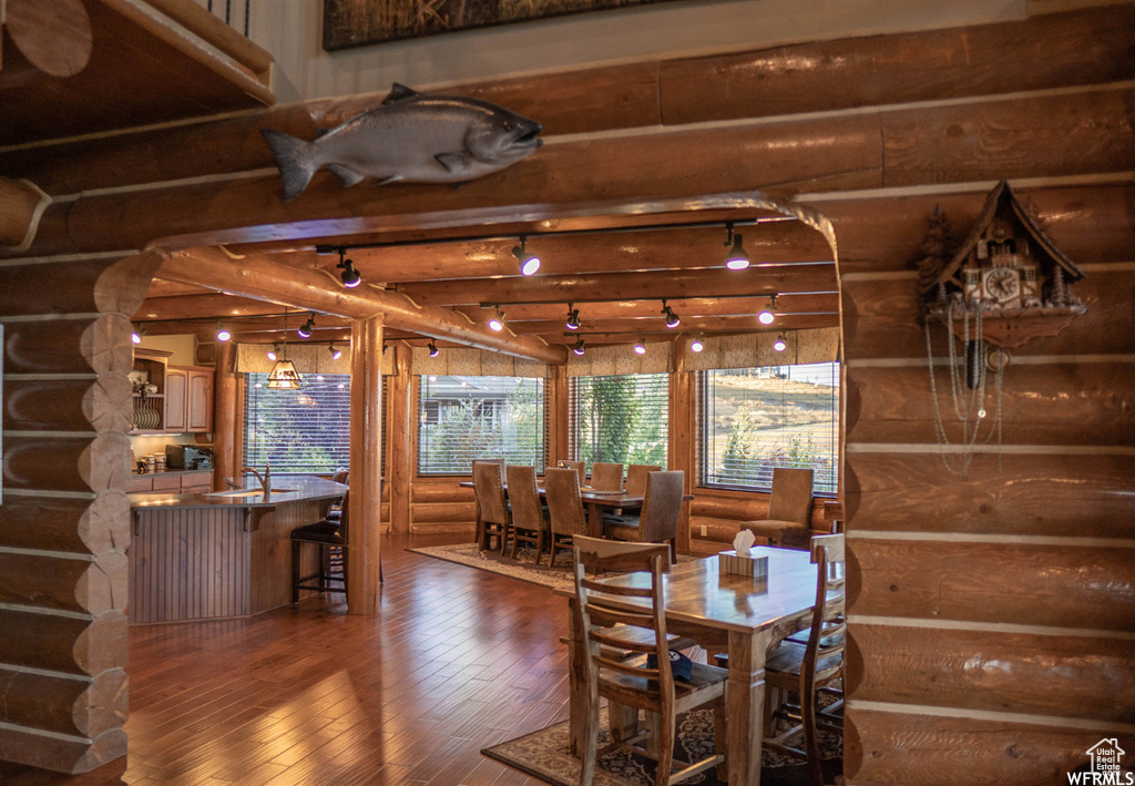 Dining room featuring dark wood-type flooring, beam ceiling, log walls, and sink