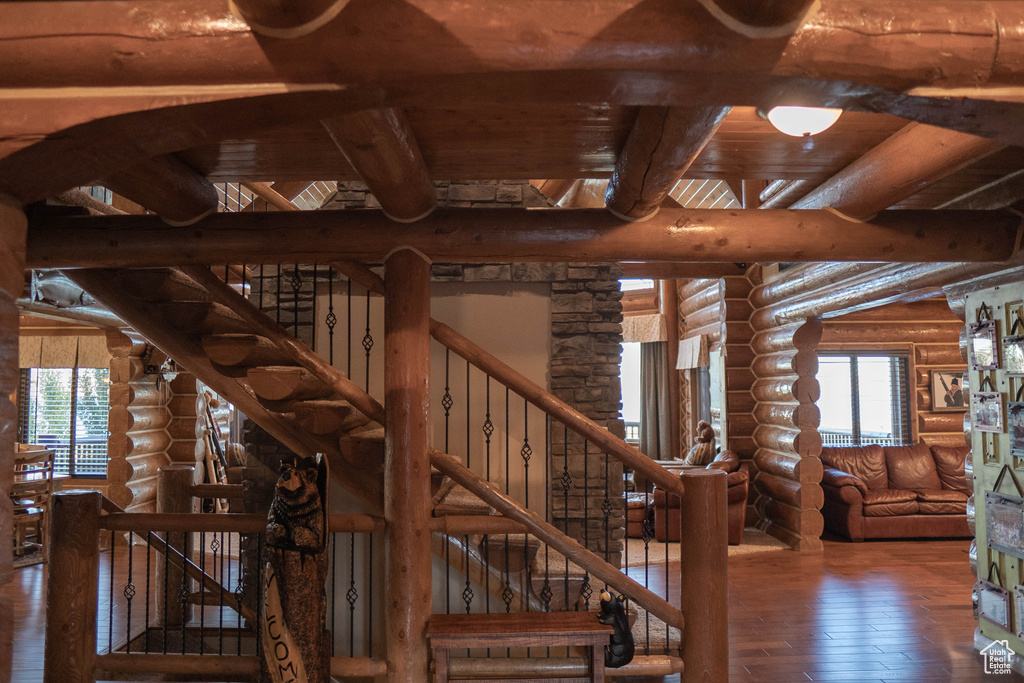 Staircase with log walls, beamed ceiling, wood ceiling, and dark wood-type flooring