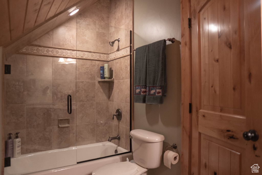 Bathroom with combined bath / shower with glass door, vaulted ceiling, and toilet