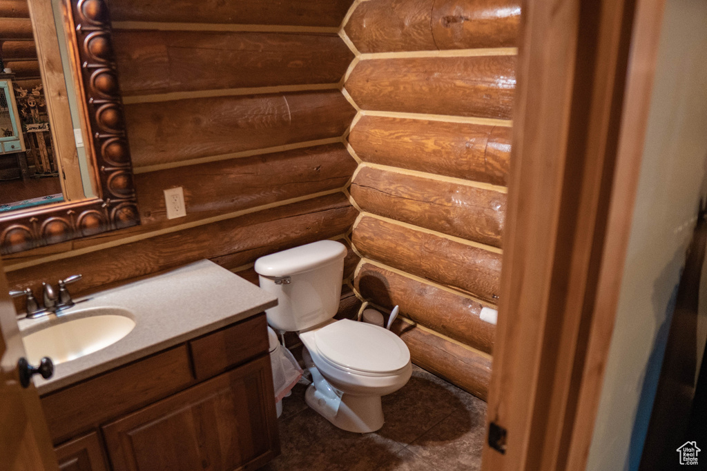 Bathroom with tile flooring, oversized vanity, log walls, and toilet