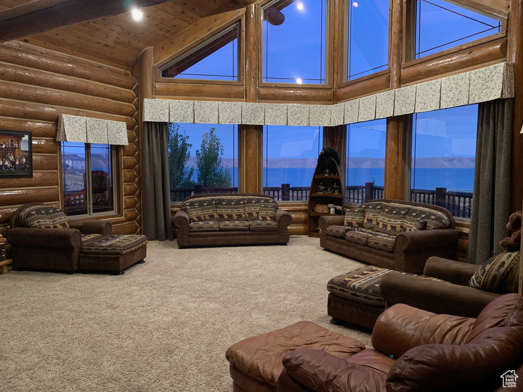 Carpeted living room featuring high vaulted ceiling, log walls, wooden ceiling, and a water view