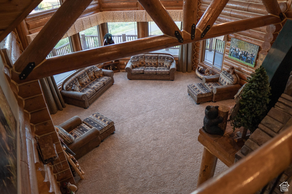 Living room featuring a wealth of natural light, vaulted ceiling with beams, carpet flooring, and rustic walls