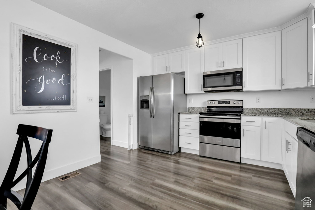 Kitchen featuring white cabinets, stainless steel appliances, hanging light fixtures, and dark wood-type flooring