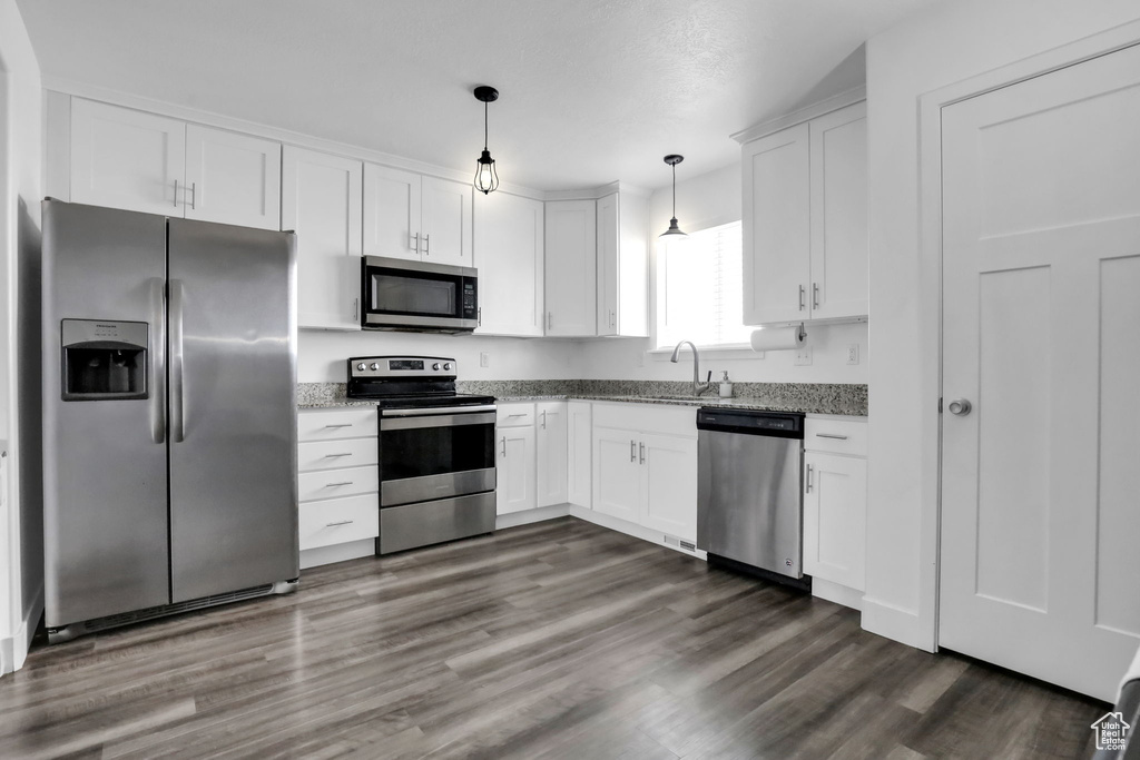 Kitchen featuring dark wood-type flooring, white cabinets, stainless steel appliances, and decorative light fixtures
