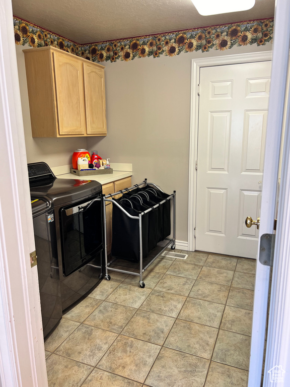 Clothes washing area with light tile floors, cabinets, and washer and clothes dryer