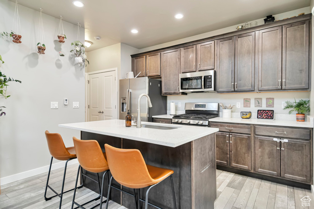 Kitchen featuring light wood-type flooring, stainless steel appliances, a center island with sink, and a breakfast bar area
