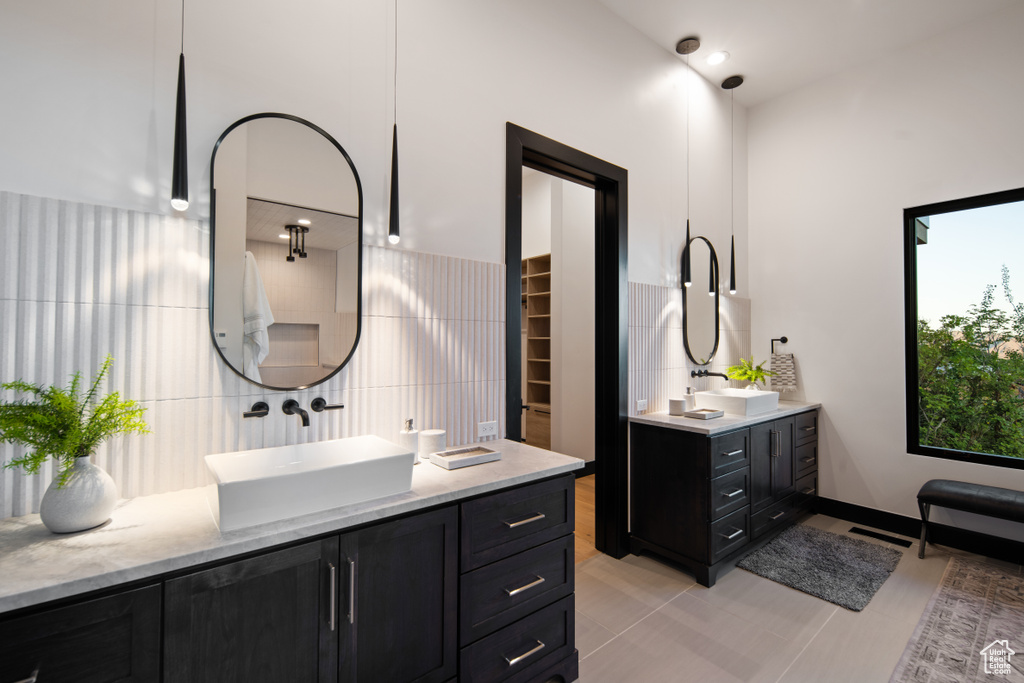 Bathroom featuring dual bowl vanity, tile flooring, tasteful backsplash, and tile walls