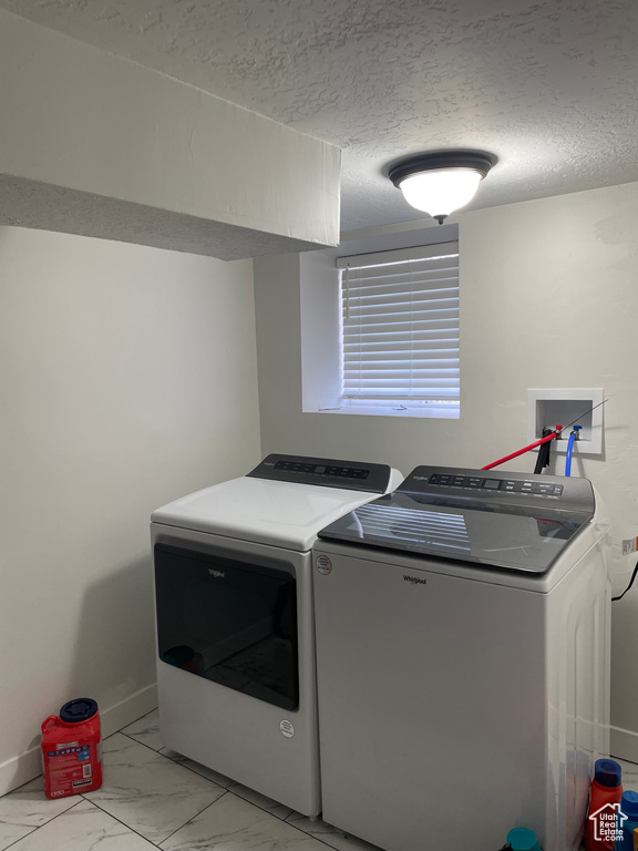 Clothes washing area with washing machine and dryer, hookup for a washing machine, a textured ceiling, and light tile floors