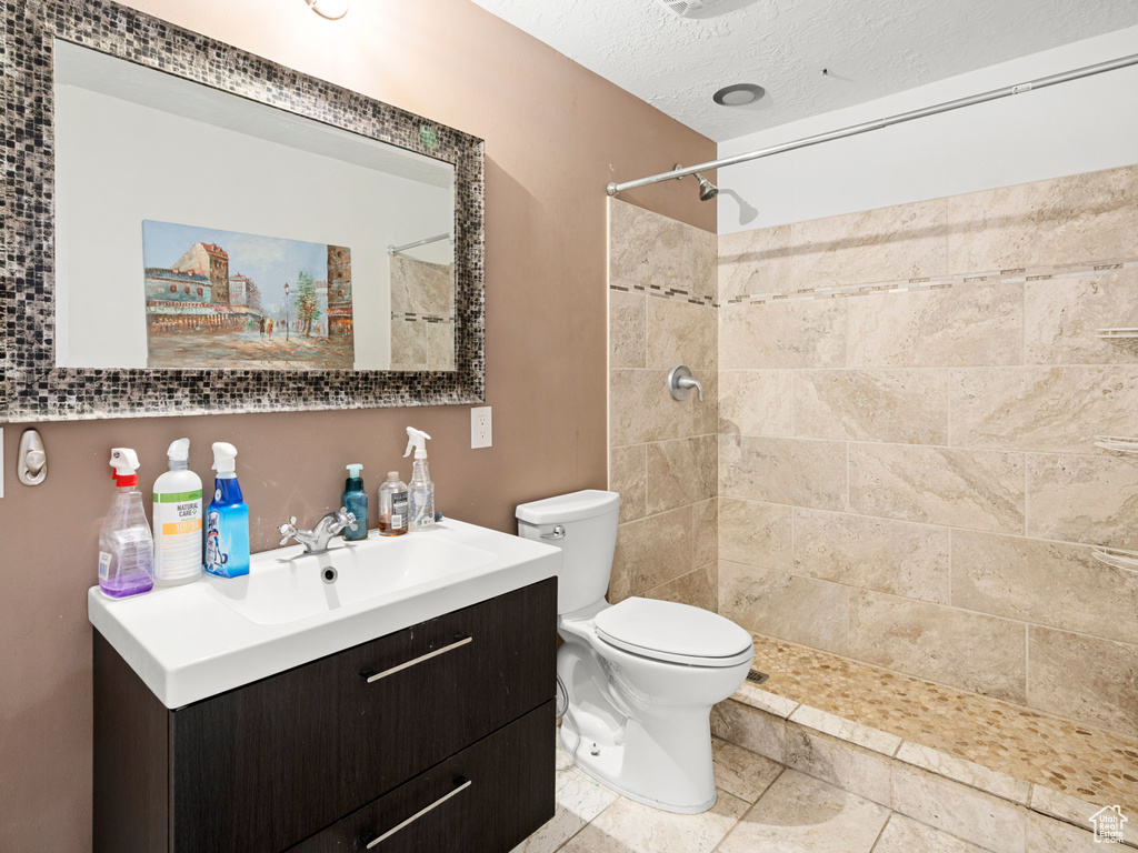 Bathroom with vanity with extensive cabinet space, a textured ceiling, tiled shower, toilet, and tile flooring