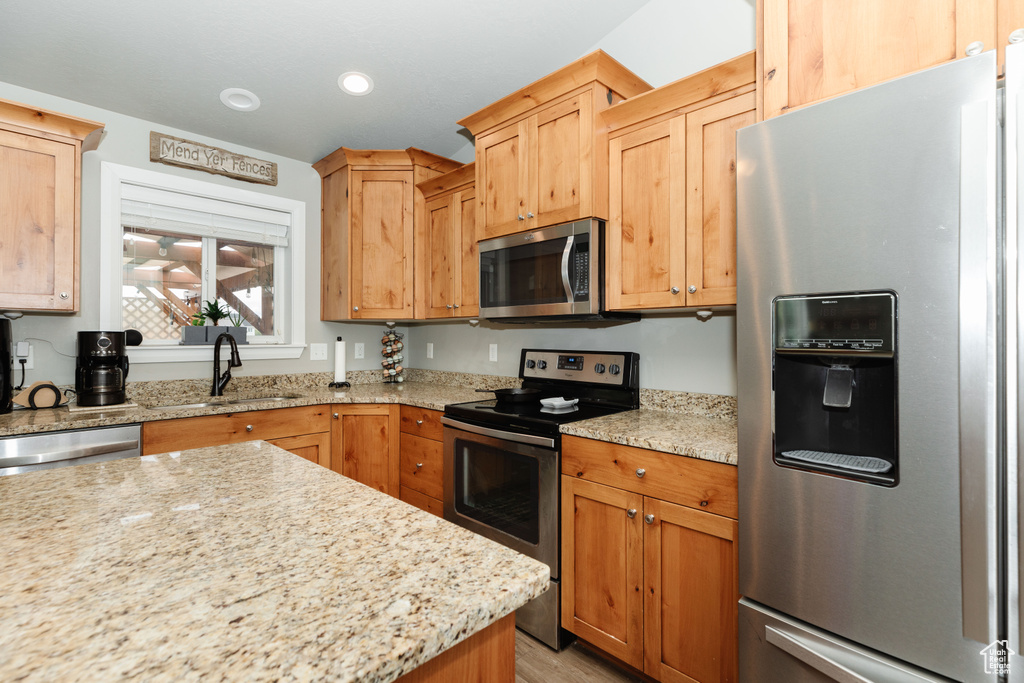 Kitchen with appliances with stainless steel finishes, light stone counters, and sink