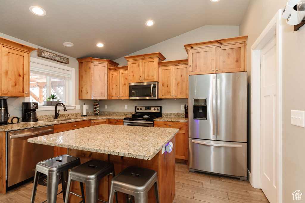 Kitchen with appliances with stainless steel finishes, a kitchen island, light stone counters, and vaulted ceiling