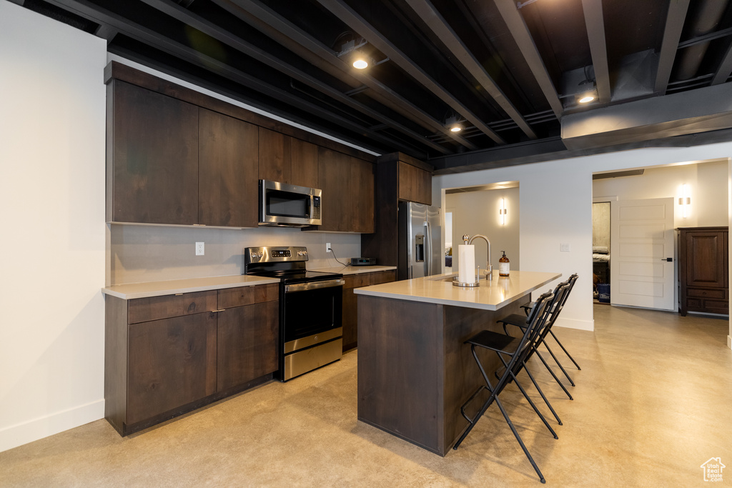 Kitchen with a center island with sink, stainless steel appliances, sink, a breakfast bar area, and dark brown cabinets