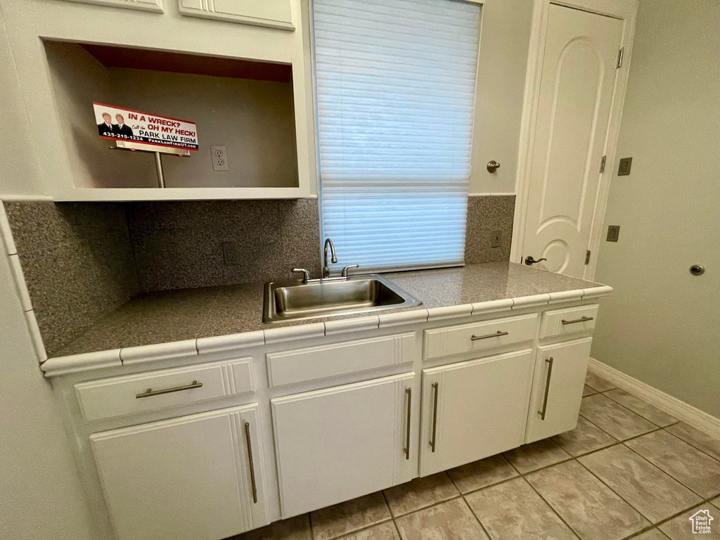 Kitchen with backsplash, tile countertops, light tile flooring, white cabinetry, and sink