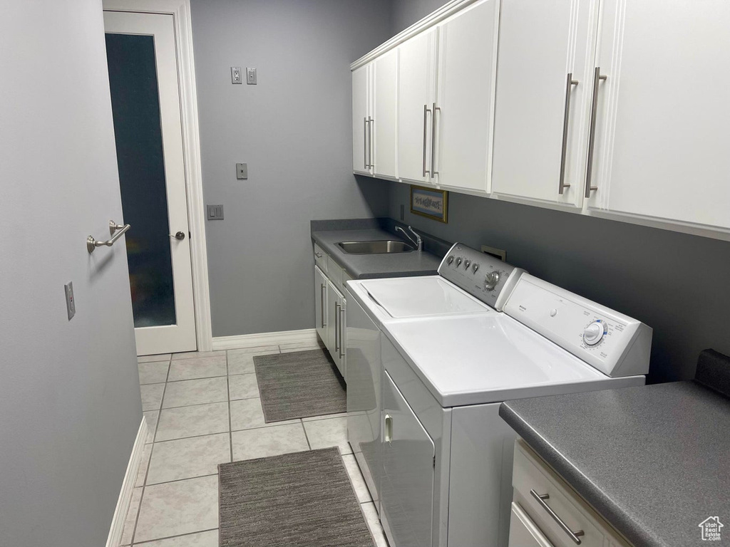 Clothes washing area with sink, cabinets, light tile floors, and washer and dryer