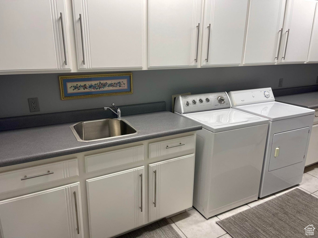 Washroom featuring light tile flooring, washer and dryer, sink, and cabinets