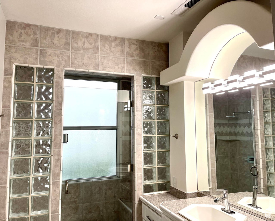 Bathroom with a shower with door, tile walls, and vanity