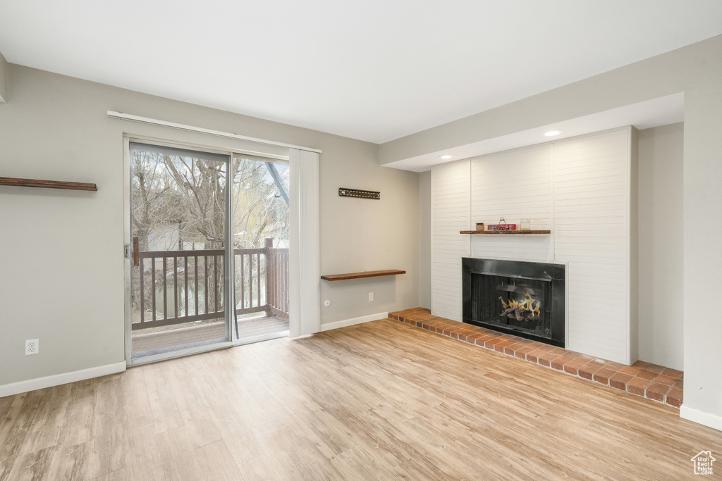 Unfurnished living room with brick wall, a brick fireplace, and light wood-type flooring